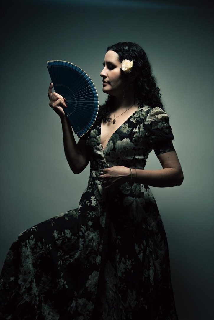 Raquel Palacios Vega in a floral dress with a white flower in her hair, holding a blue fan